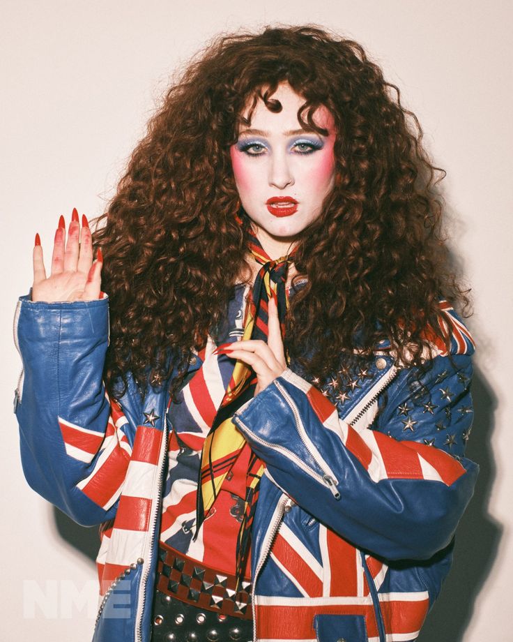 a woman with red hair and makeup is wearing a union jack jacket while holding her hands in the air