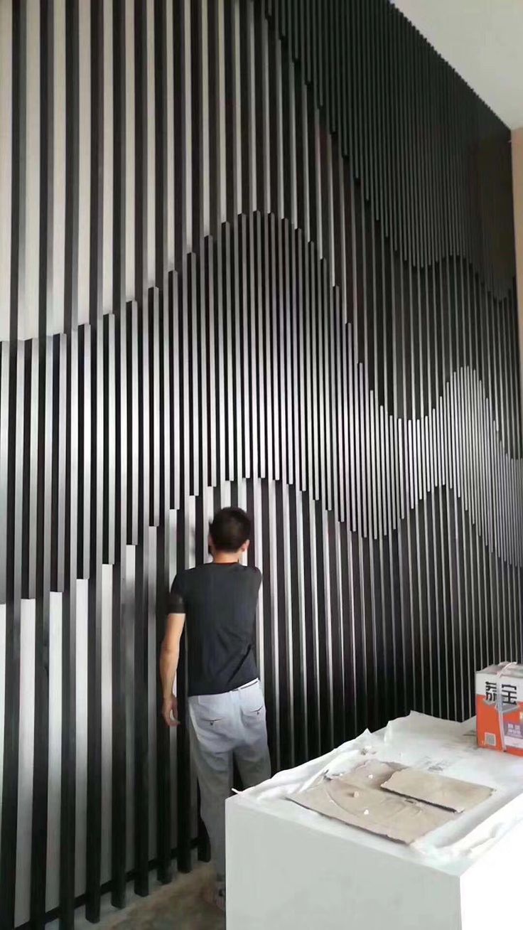 a man standing in front of a wall made out of black and white vertical strips