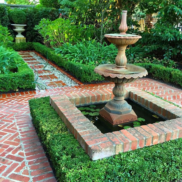 a fountain in the middle of a garden surrounded by greenery and brick walkways