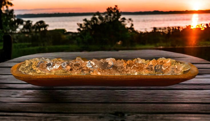 a wooden table topped with a glass bowl filled with crystal stones next to the ocean