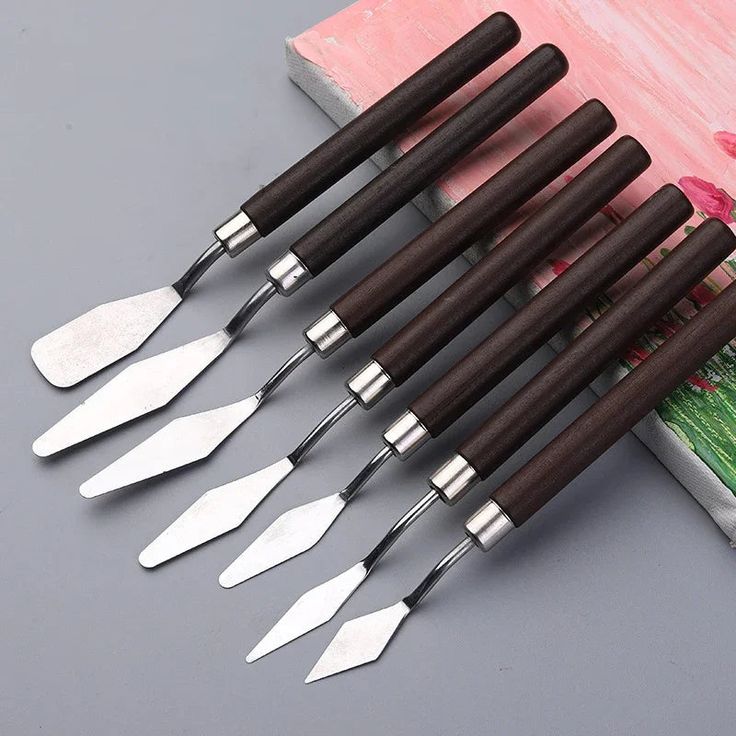 six pieces of wood and metal cooking utensils on a gray surface with pink flowers in the background