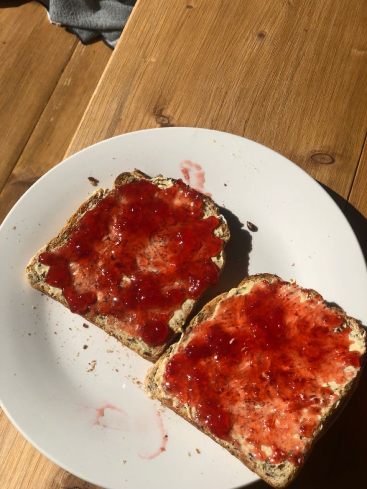 two pieces of bread with ketchup on them sitting on a white plate next to a wooden table