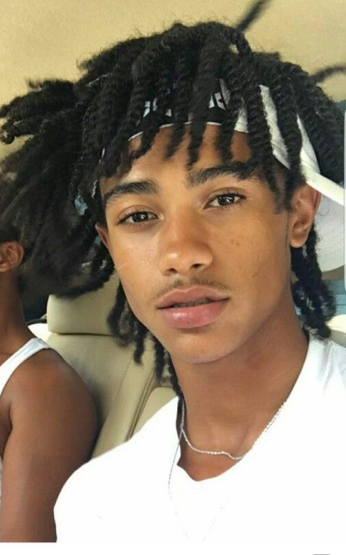 a young man with dreadlocks sitting in the back seat of a car looking at the camera