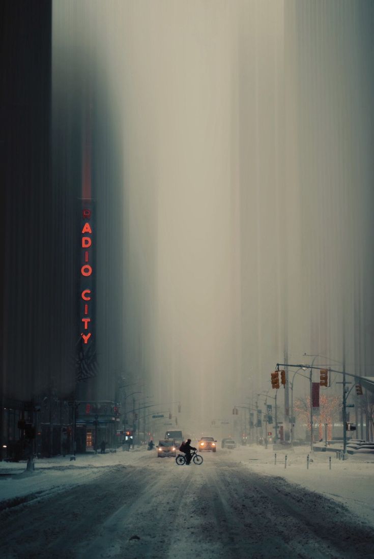 a car driving down a snow covered road next to tall buildings and traffic lights in the distance