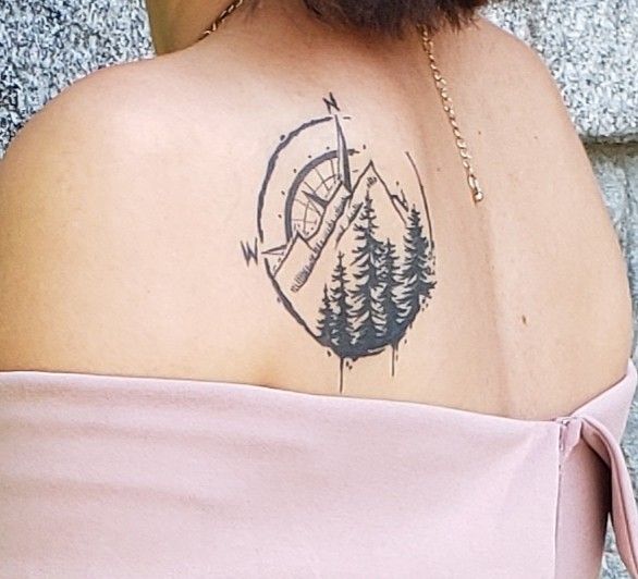 the back of a woman's shoulder with a compass and trees tattoo on it