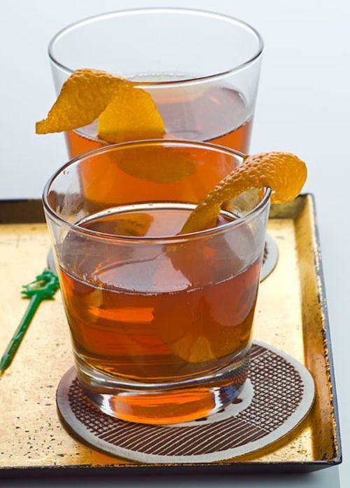 two glasses filled with liquid and orange peels on a metal tray next to each other