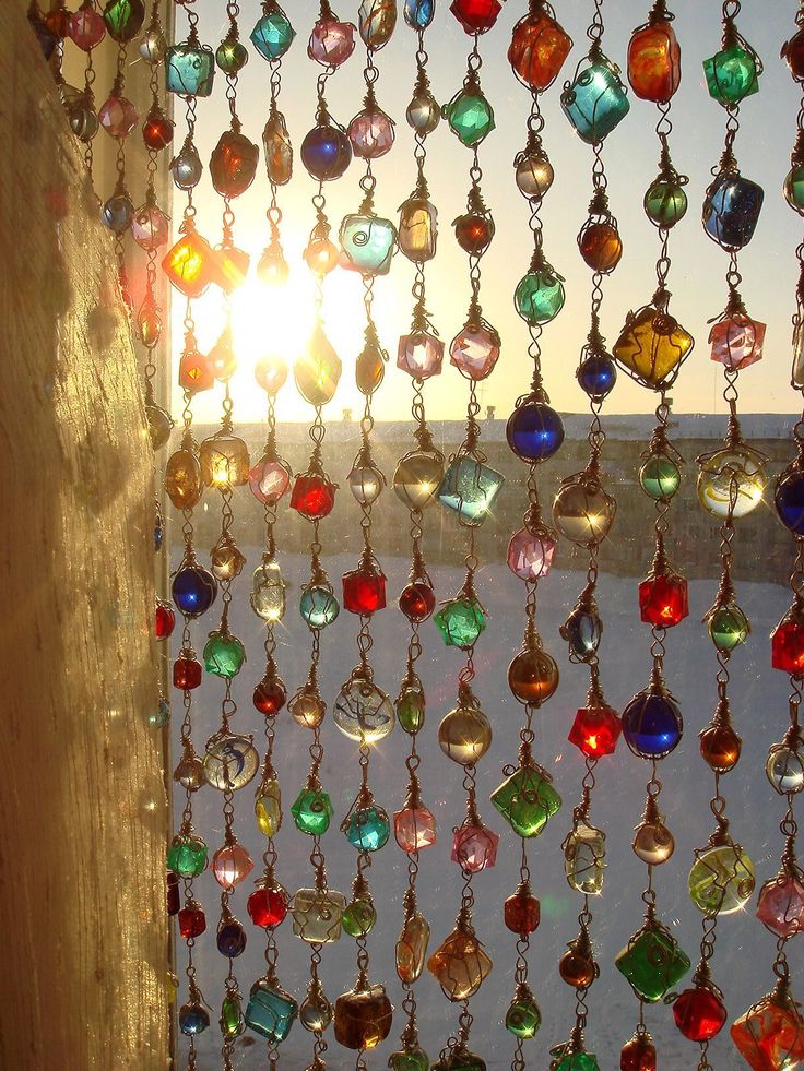 the sun shines through an open window with colorful glass beads hanging from it's sides