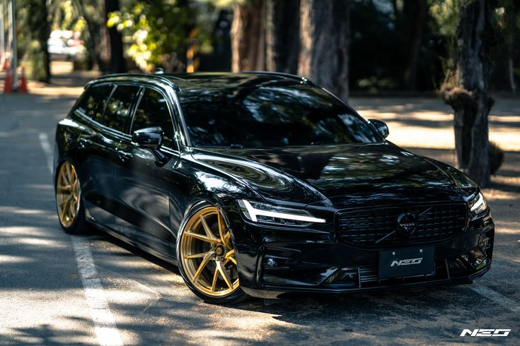 a black car parked on the side of a road next to trees and orange cones