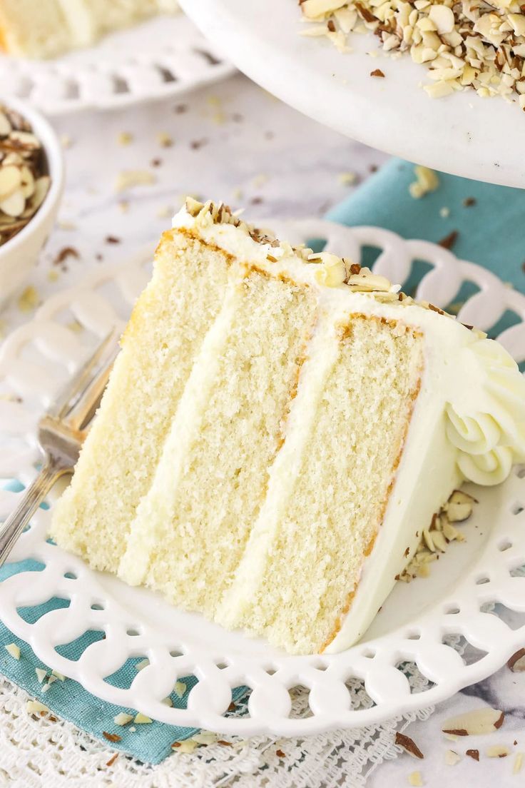 a slice of white cake on a plate with a fork and bowl of nuts in the background