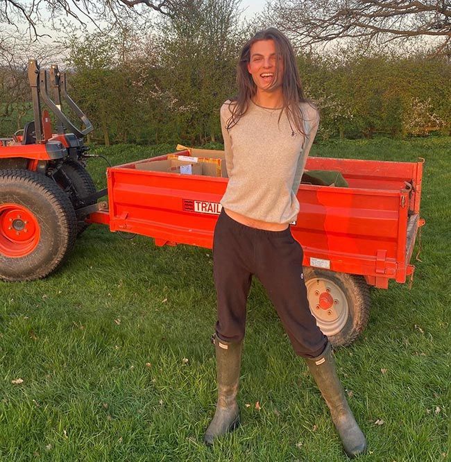 a woman standing in front of a red trailer with an orange tractor behind her on the grass