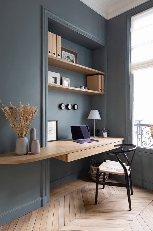 a desk with a laptop computer on top of it next to a chair and window