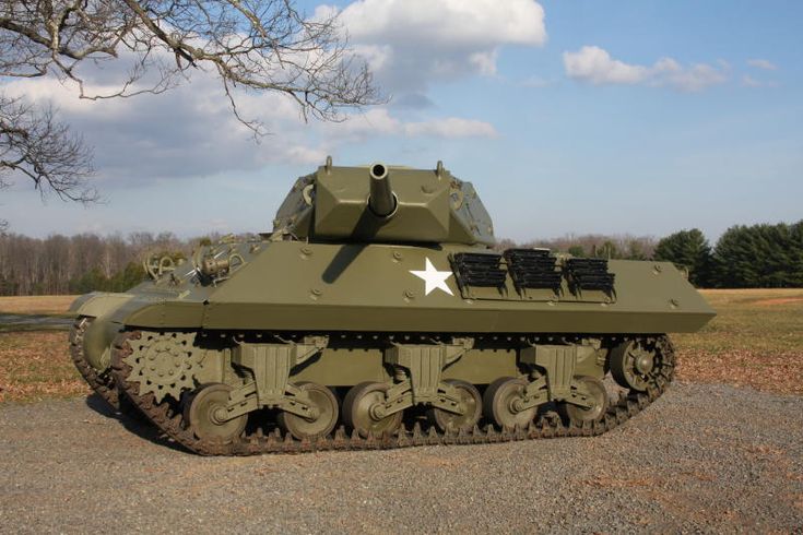 an army tank sitting on top of a gravel road next to a tree and grass covered field