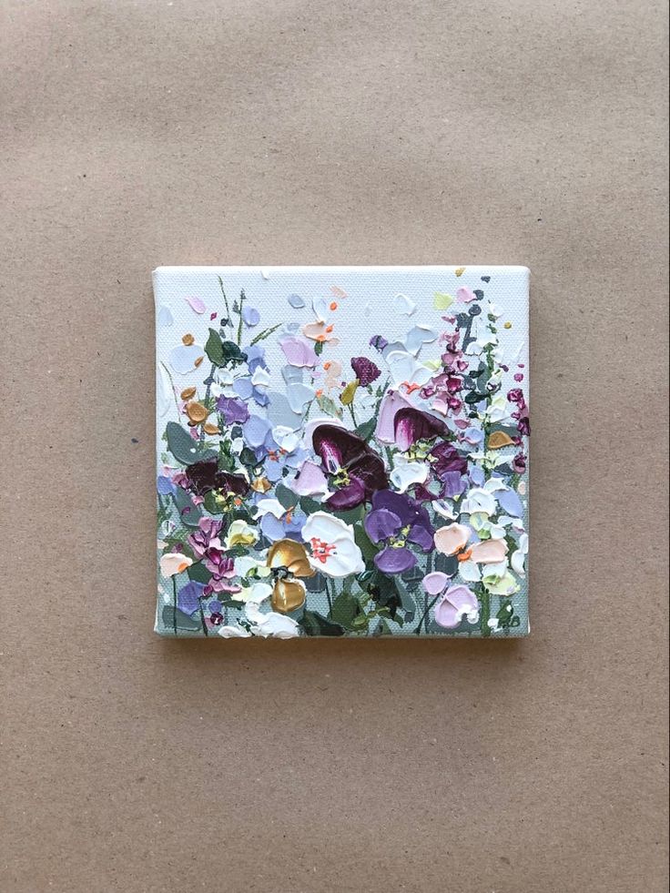 a square tile with flowers painted on it's side, sitting on a brown surface