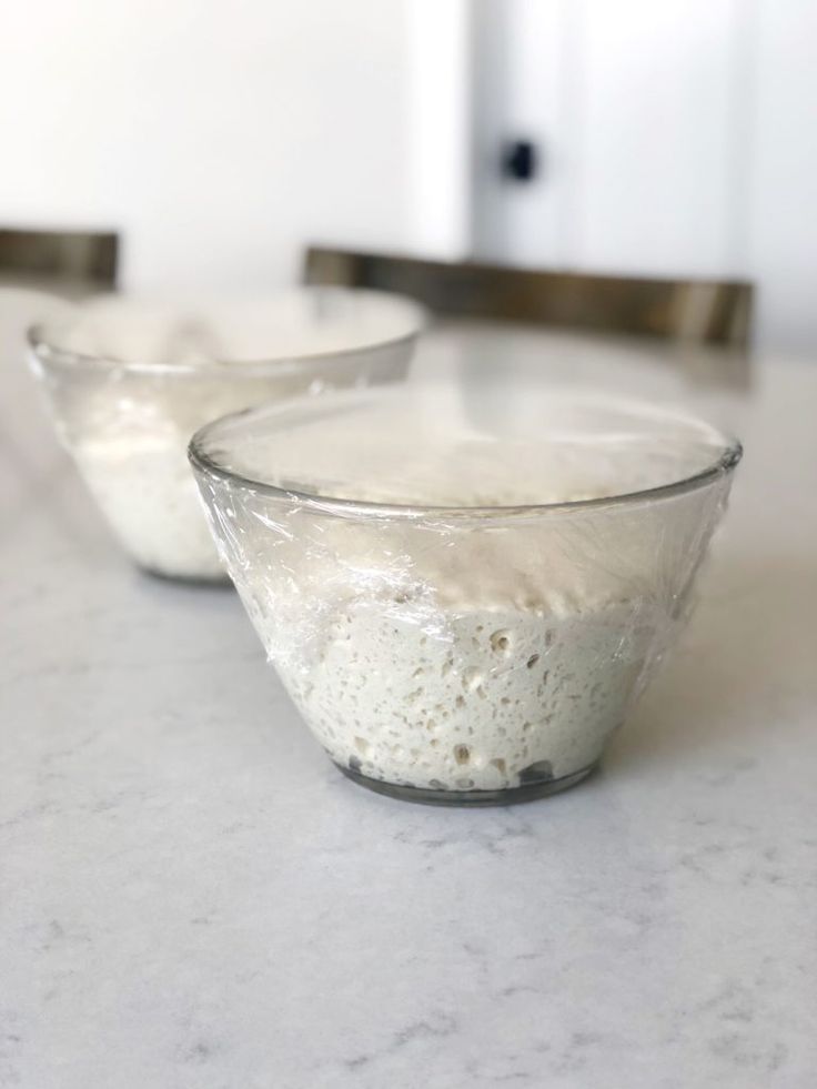 two glass bowls filled with food sitting on top of a white marble countertop next to each other