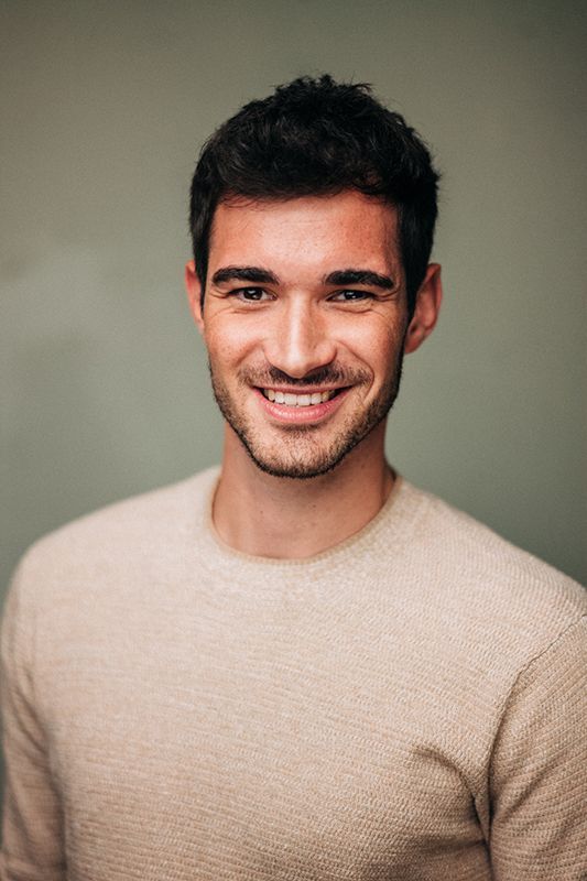 a smiling man in a tan sweater is looking at the camera with a smile on his face