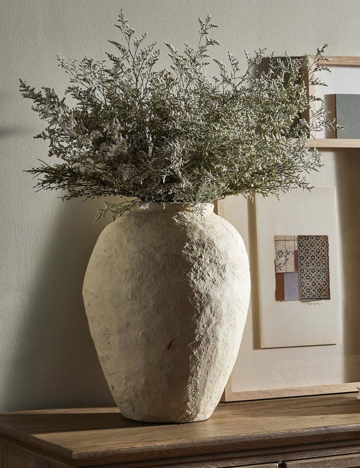 a white vase sitting on top of a wooden table next to a framed photo and flowers