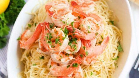 pasta with shrimp and parsley in a white bowl next to lemon wedges on the side