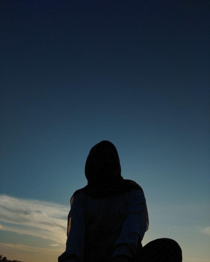 a person sitting on the ground with their skateboard in front of them at sunset