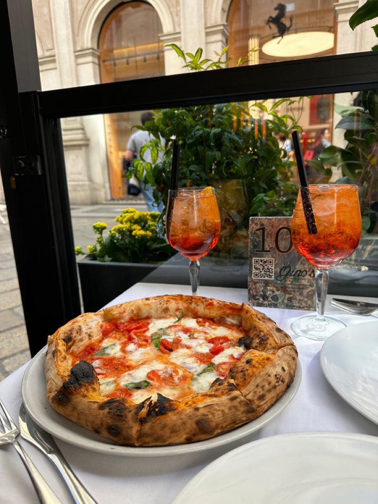 a pizza sitting on top of a white plate next to two glasses of red wine