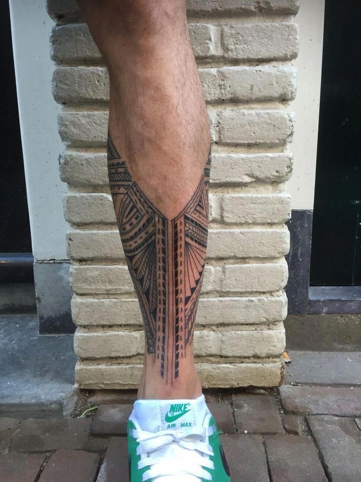 a man's leg with a tattoo on it and his green sneakers in front of a brick wall