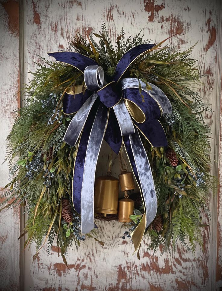 a christmas wreath with bells hanging on the front door, decorated with evergreen and blue ribbon