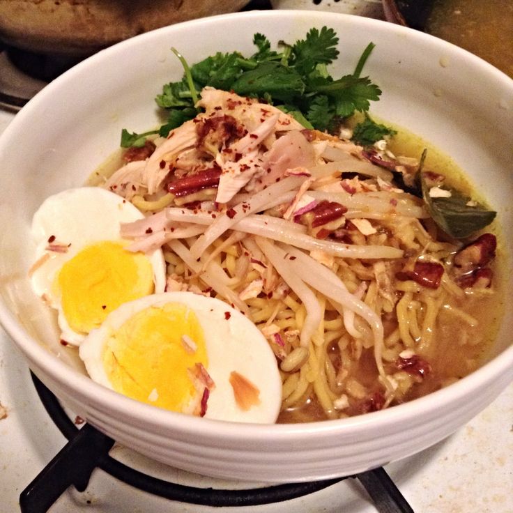 a white bowl filled with noodles, meat and eggs on top of a stovetop