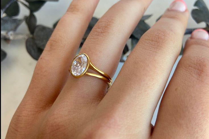 a woman's hand wearing a gold ring with a white diamond on the side