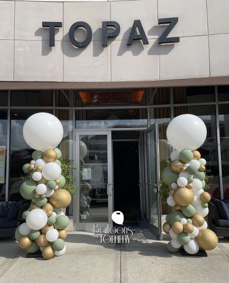 two tall white and gold balloons are in front of a topaz store with the words topaz on it