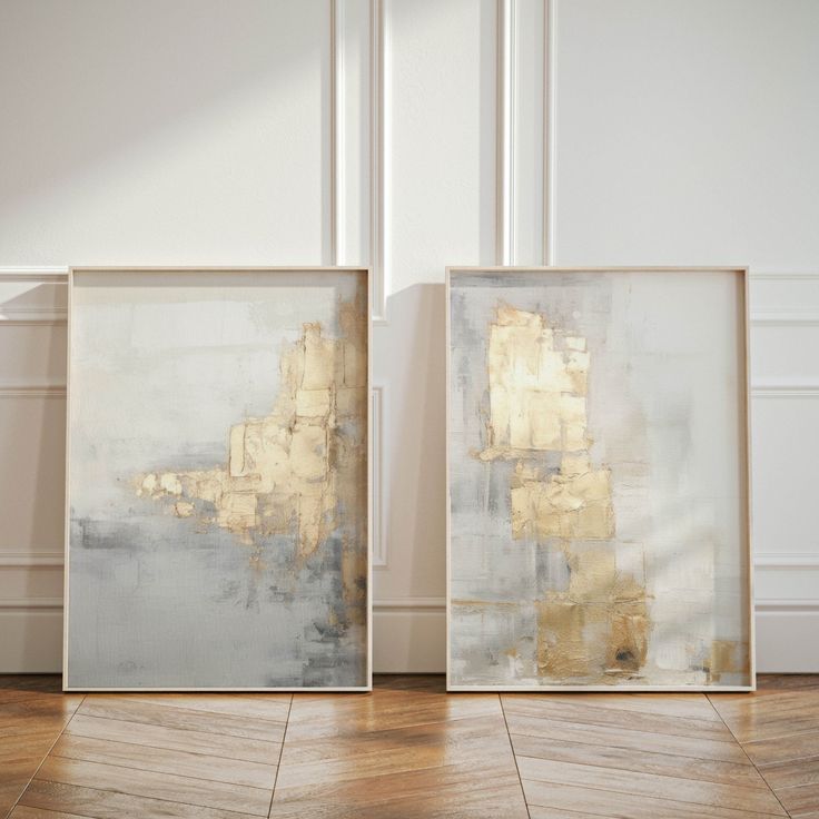 two framed paintings on the floor in front of a wall with white and gold paint