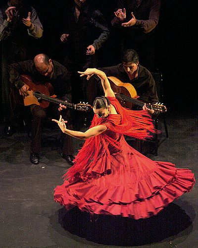 a woman in a red dress is dancing on stage with other people and musicians behind her