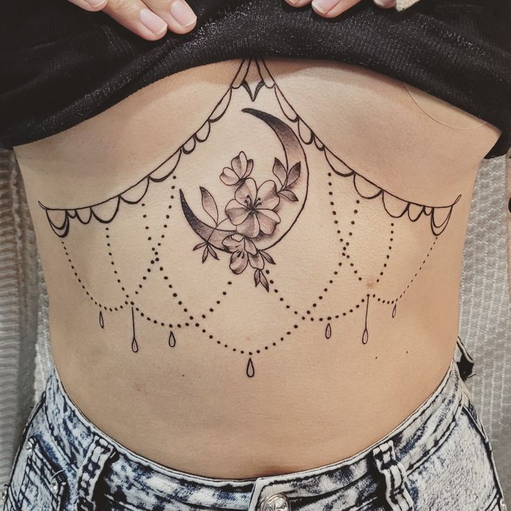 a woman's stomach with a flower and moon tattoo on her belly, which is decorated with beads