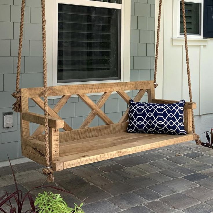 a wooden porch swing sitting on top of a brick patio next to a door and window