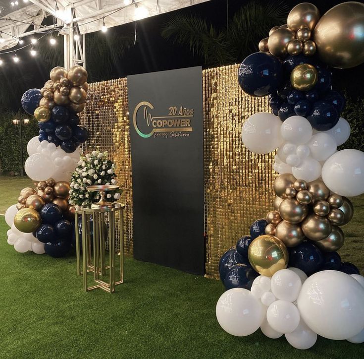 an outdoor event with balloons and decorations on the grass in front of a gold wall