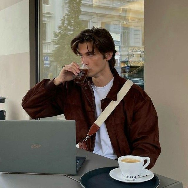 a man sitting at a table drinking from a glass in front of a laptop computer