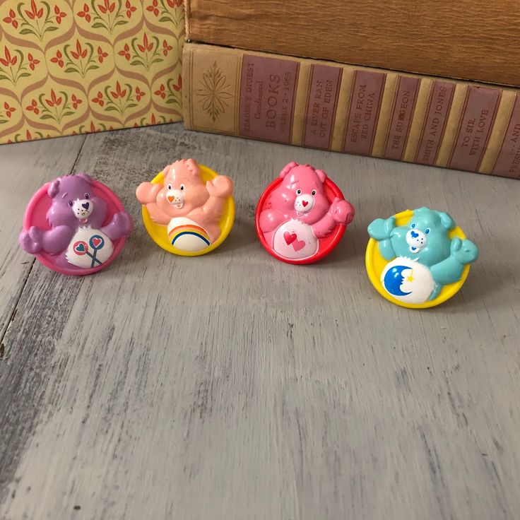 three small toy bears sitting on top of a wooden table next to a bookshelf