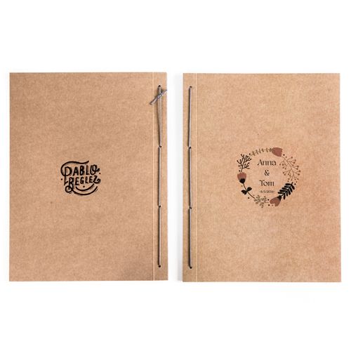 two brown notebooks sitting side by side on top of each other, one with a pen in it