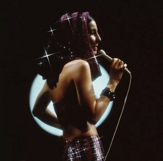 a woman in a disco outfit holding a microphone and looking at her reflection on the mirror