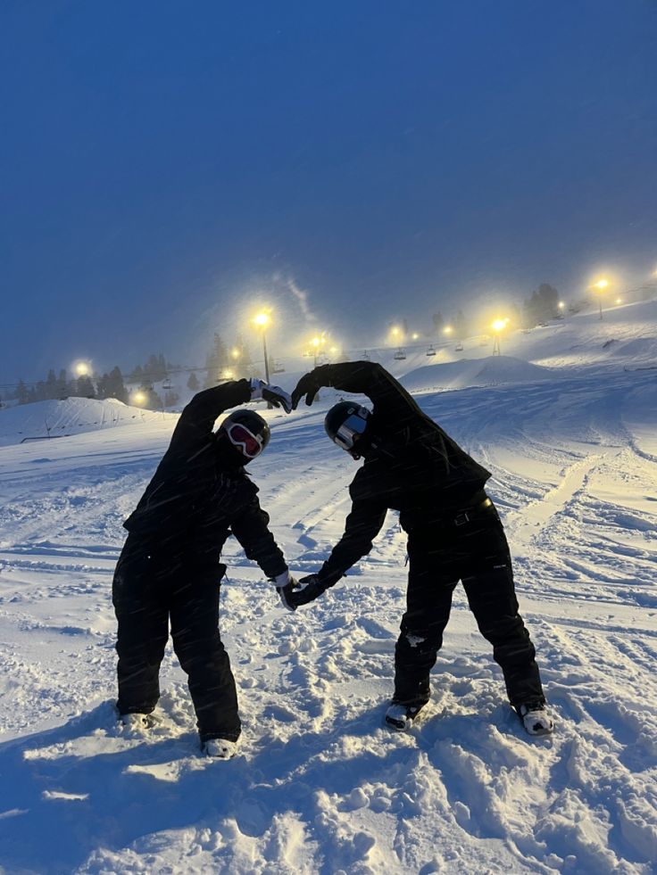 two people standing in the snow making a heart shape with their hands and holding each other's hand