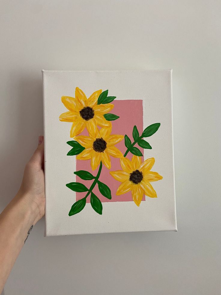 a person holding up a painting with yellow flowers on it