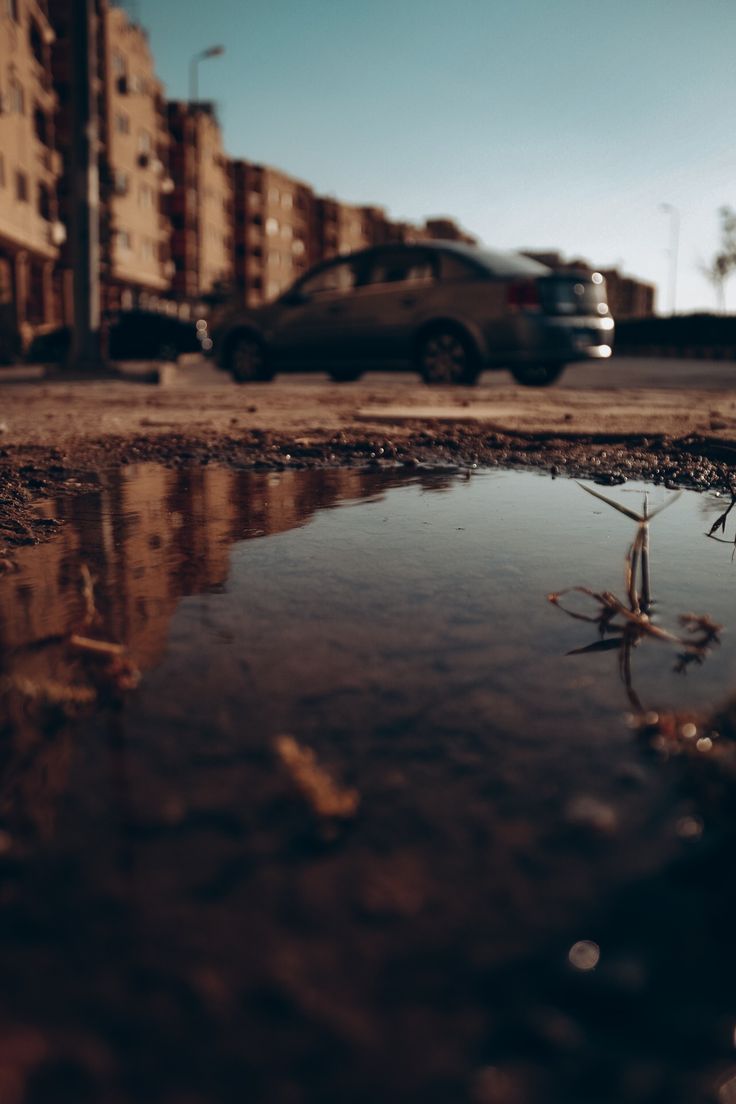 a car is parked on the street next to a puddle