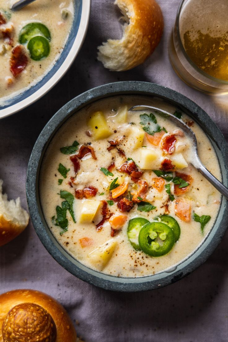 two bowls filled with soup next to some bread and other food on a table top