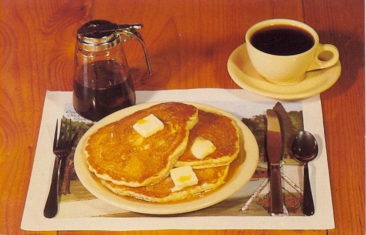 pancakes with butter and syrup are on a plate next to a cup of coffee, spoons and utensils