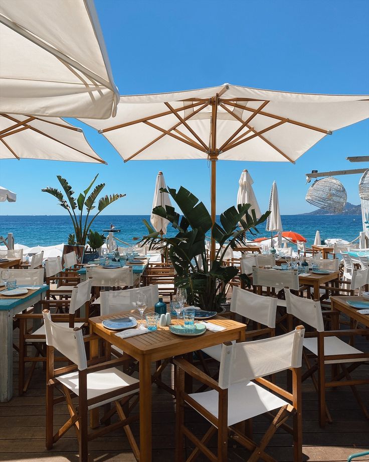 an outdoor dining area with tables, chairs and umbrellas overlooking the ocean on a sunny day