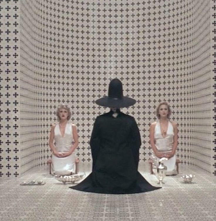 three women sitting on chairs in front of a black and white wall with an artistic pattern