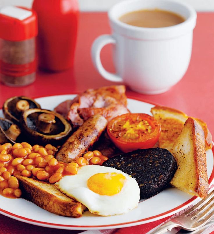 a breakfast plate with eggs, toast, beans and tomatoes on it next to a cup of coffee