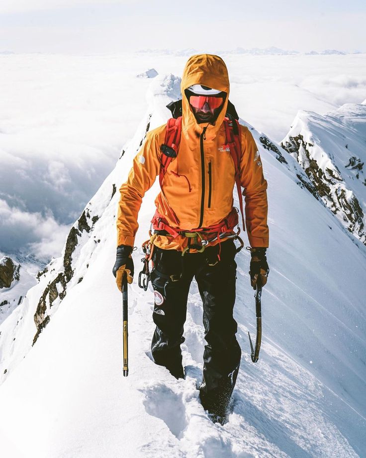 a man walking up the side of a snow covered mountain with skis and poles