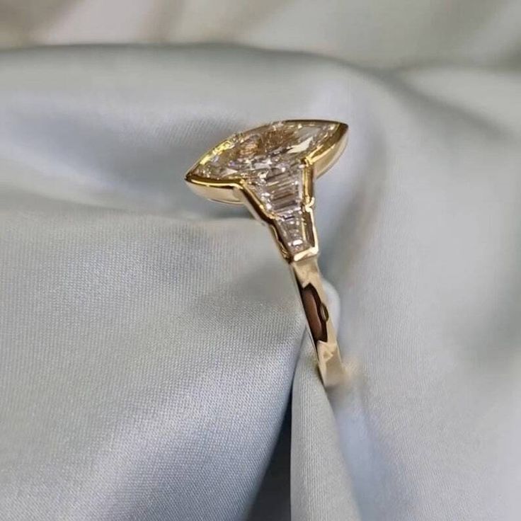 a yellow gold ring with a pear shaped diamond set in the center on a white satin background