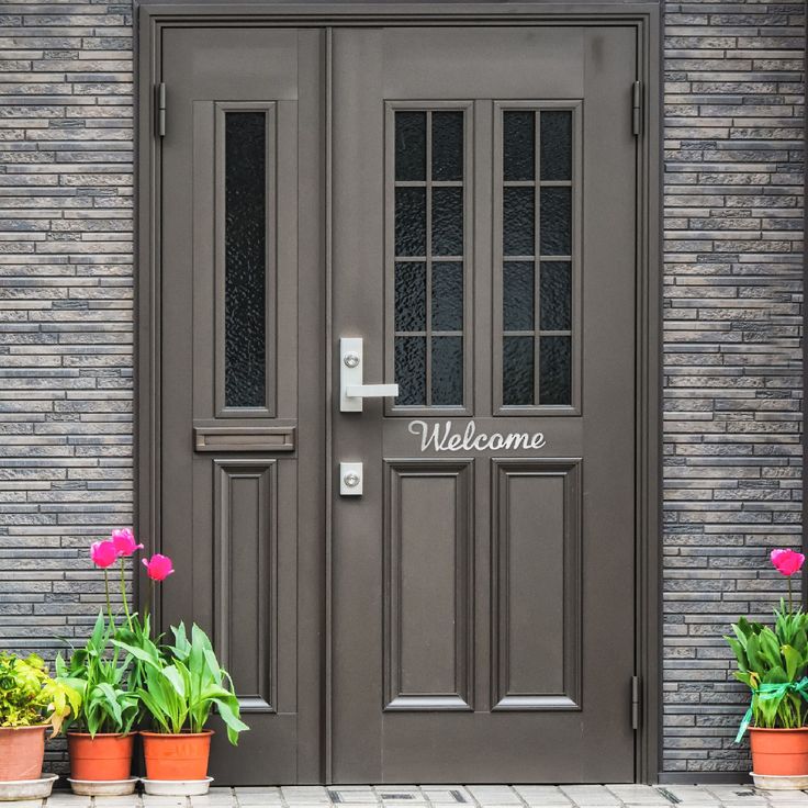 two potted plants are next to the front door and welcome sign that says welcome