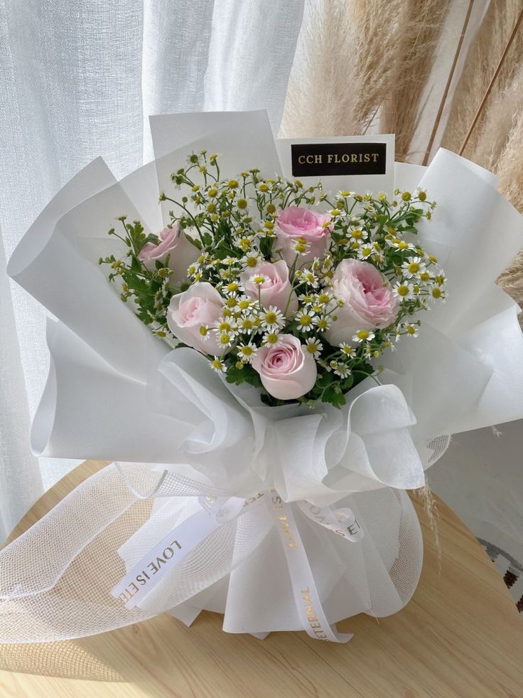 a bouquet of pink roses and baby's breath sits on a table next to a card