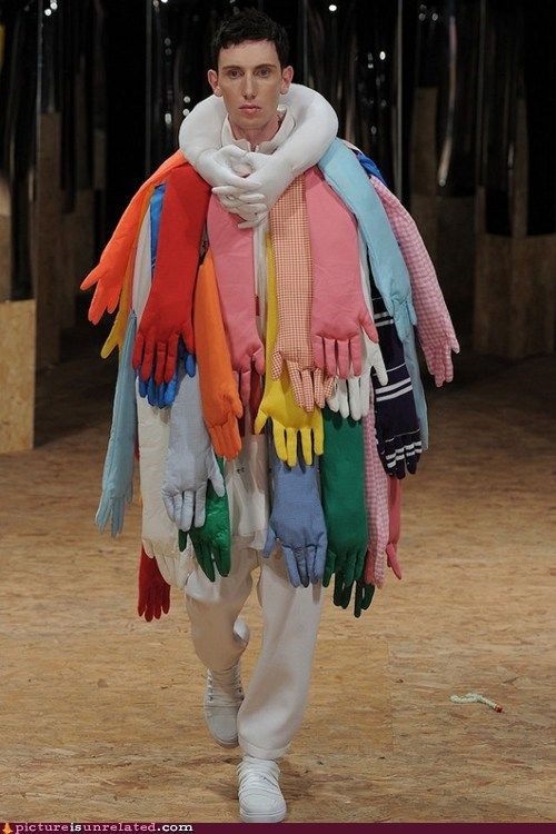 a man walking down a runway with lots of colorful gloves on his shoulders and arms